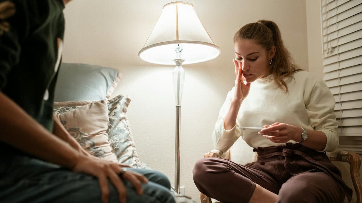 A woman reacts to a pregnancy test in a softly lit bedroom, sharing the moment with her partner.