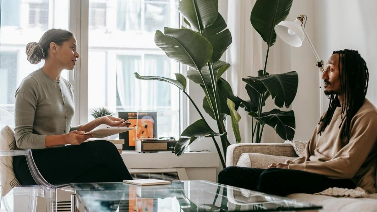 Side view of professional female African American therapist sitting in front of black male patient during psychotherapy session in office