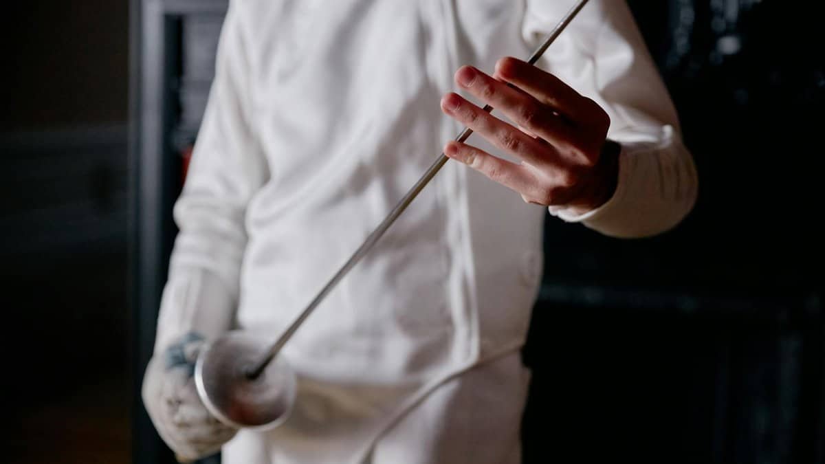 A focused view of a fencer holding a sword, ready for action in an indoor setting.