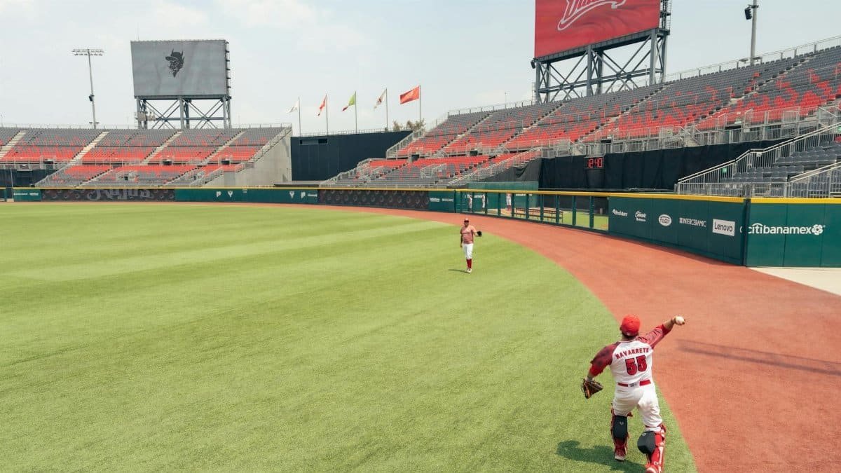 Two baseball players on field with empty bleachers in stadium setting, preparing for game.