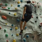 Back view of anonymous sportspeople in activewear hanging on rope after ascending climbing wall in bouldering center