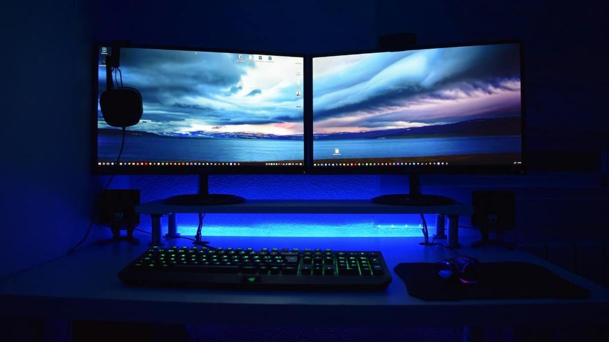 Dual monitors with blue lighting on a gaming desk setup.