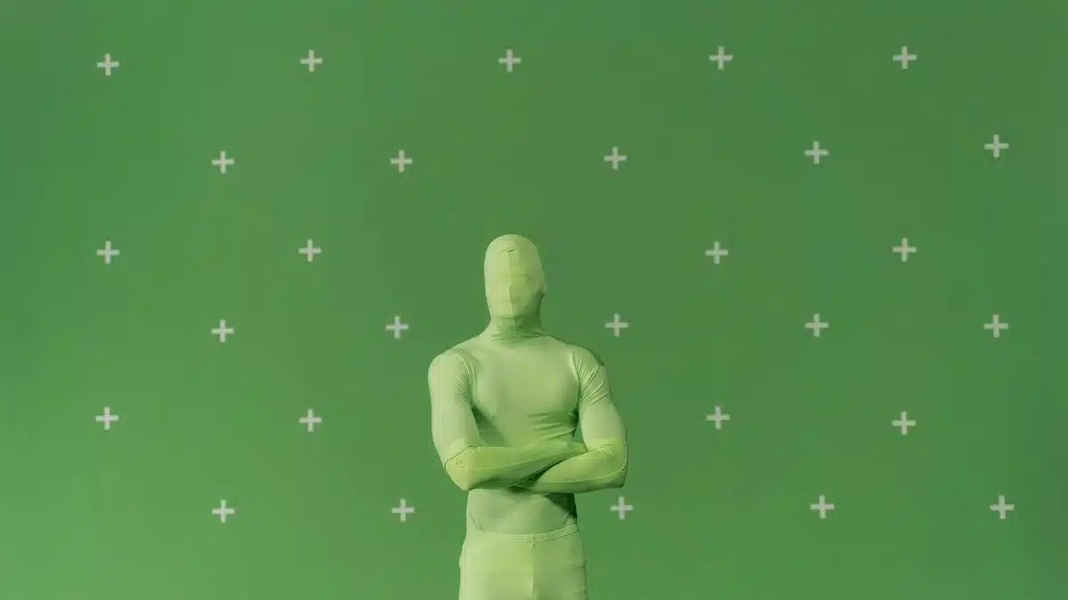 Person in a green chroma key suit standing against a marked green screen in a studio.