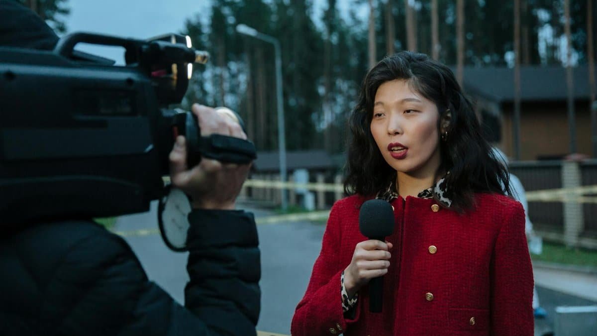 Asian female journalist reporting live from a suburban crime scene with camera and microphone.