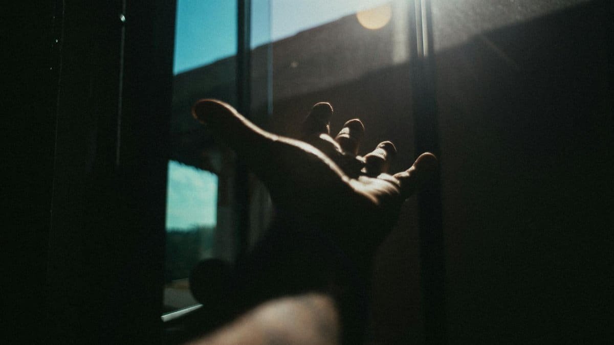 A dramatic portrayal of a hand reaching towards sunlight through a window, casting a shadow.