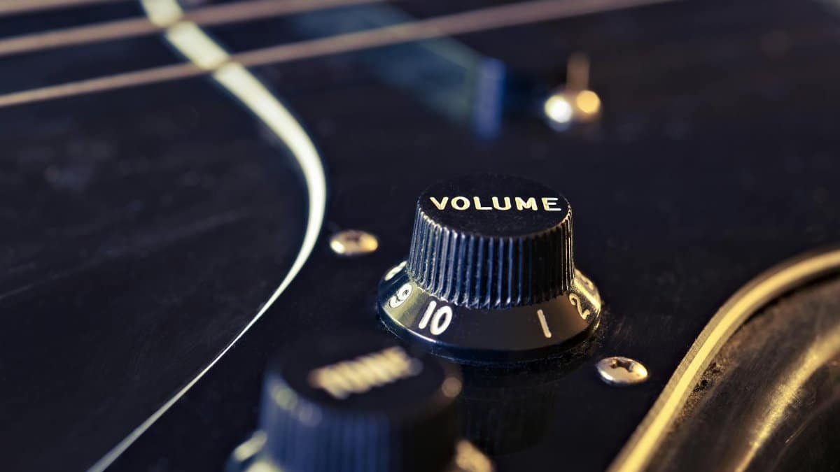 Detailed view of an electric guitar's volume knob with strings in the background.