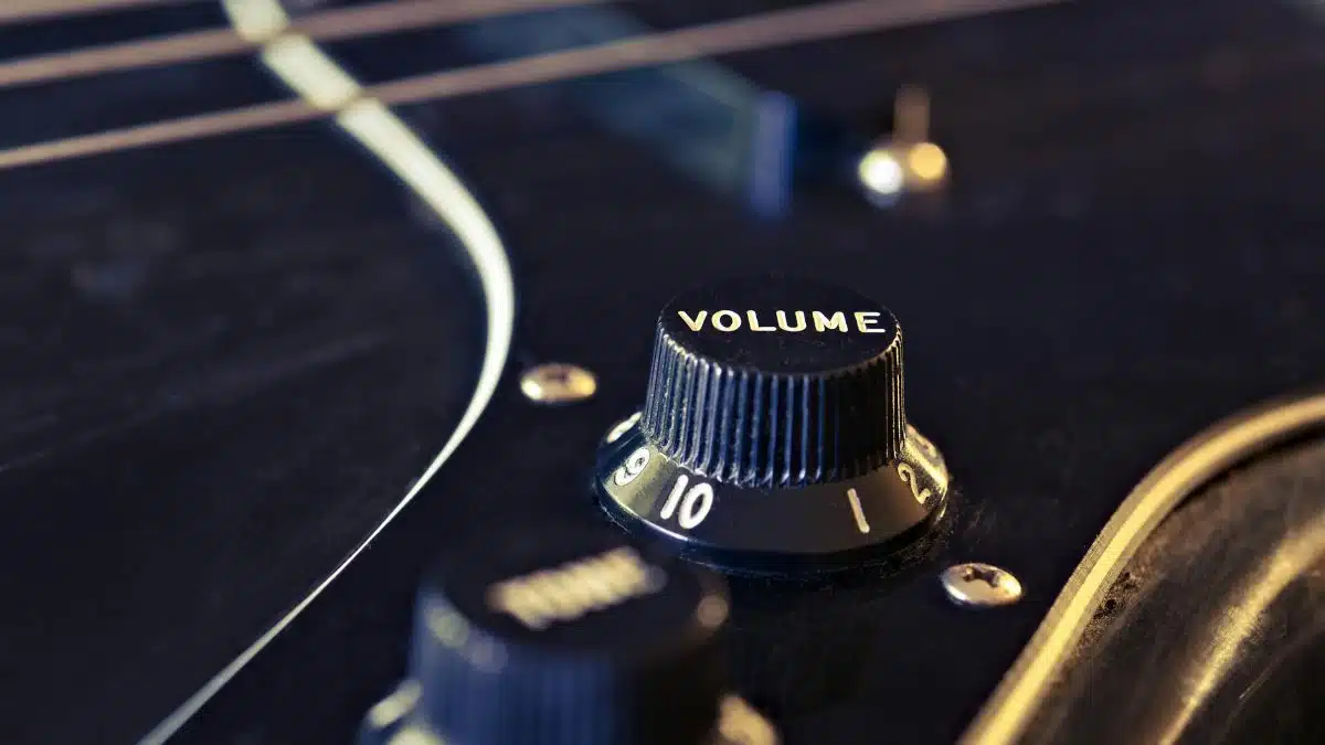 Detailed view of an electric guitar's volume knob with strings in the background.