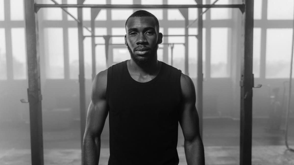 Black and white portrait of a muscular man in a gym with a strong, confident expression.