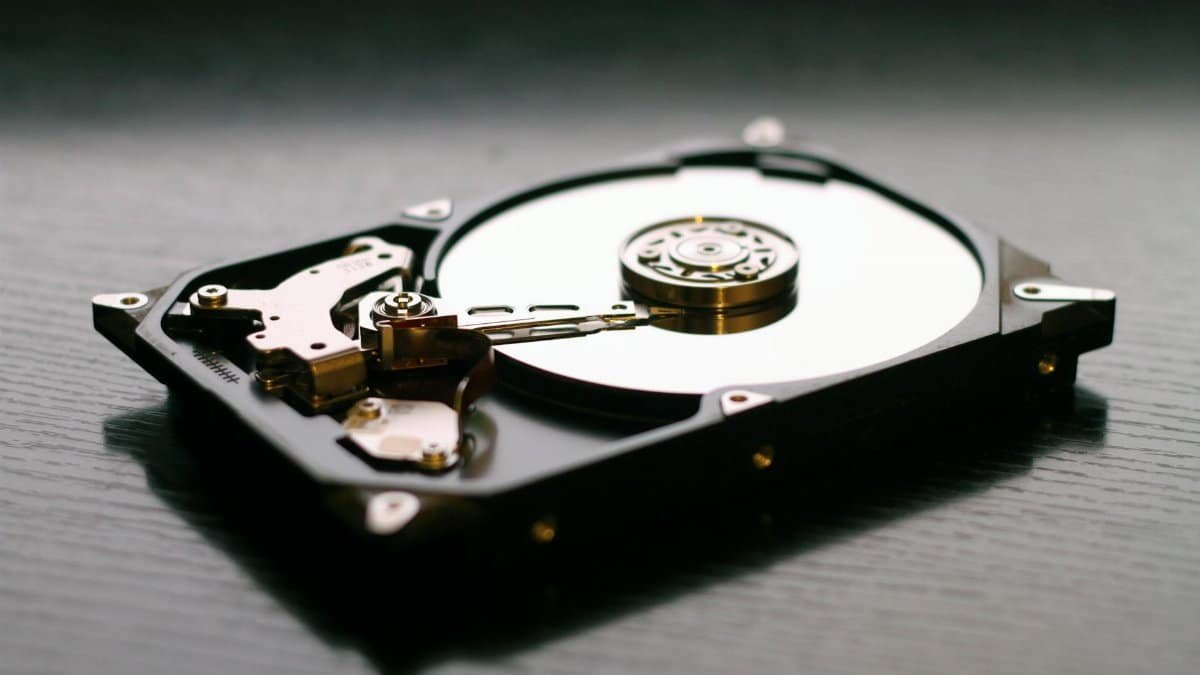 An open hard drive is displayed on a wooden surface, showcasing its internal components and metallic details.