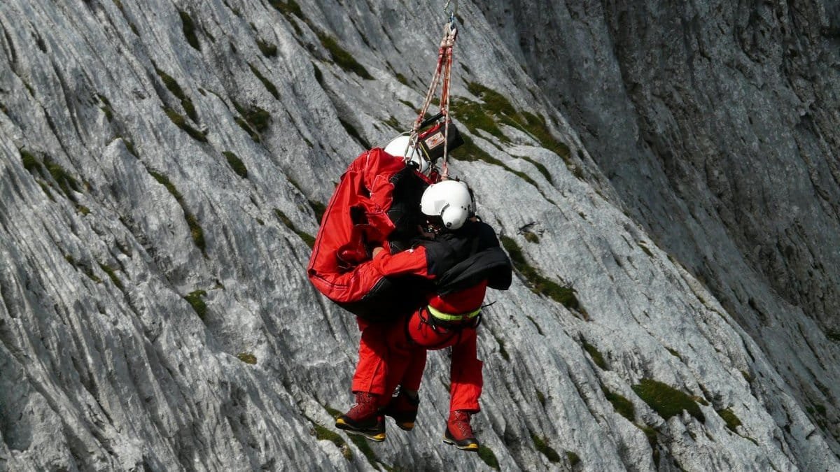 Two rescuers in action on a mountain, showcasing teamwork and safety in a daring lift.