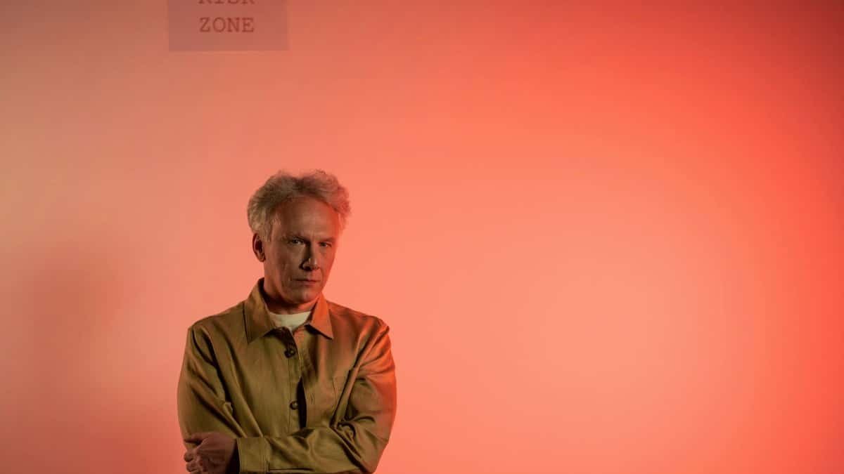 Portrait of a senior man standing indoors with a 'risk zone' warning and red background.