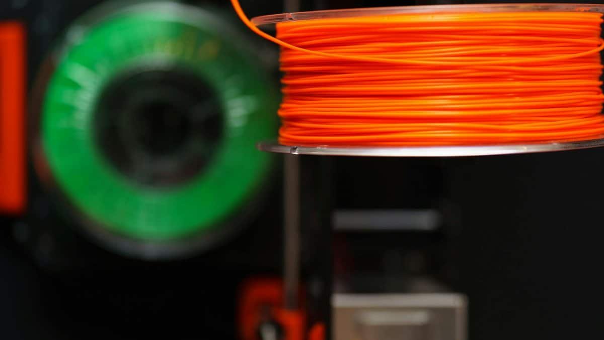 Detailed view of orange and green 3D printer filament spools, perfect for creative and industrial projects.