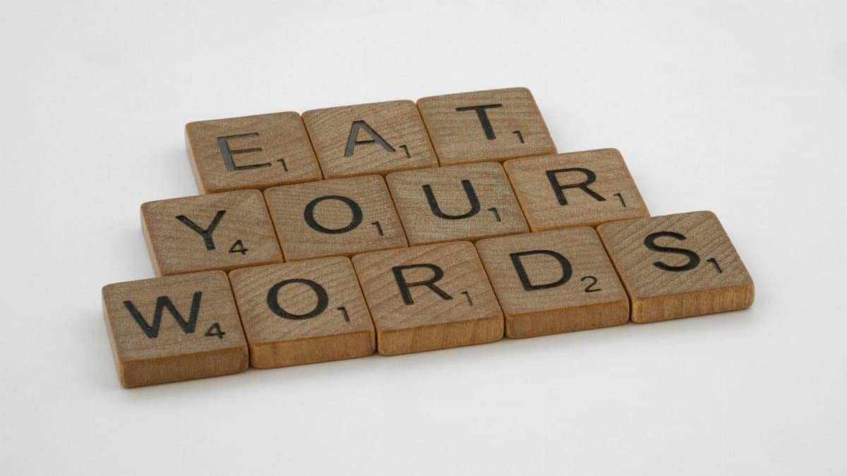 Wooden Scrabble tiles arranged to spell 'Eat Your Words' on a white background.