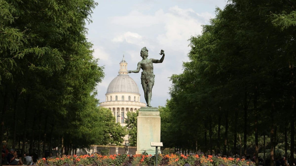 A picturesque statue framed by lush trees with Paris's Pantheon in the background.