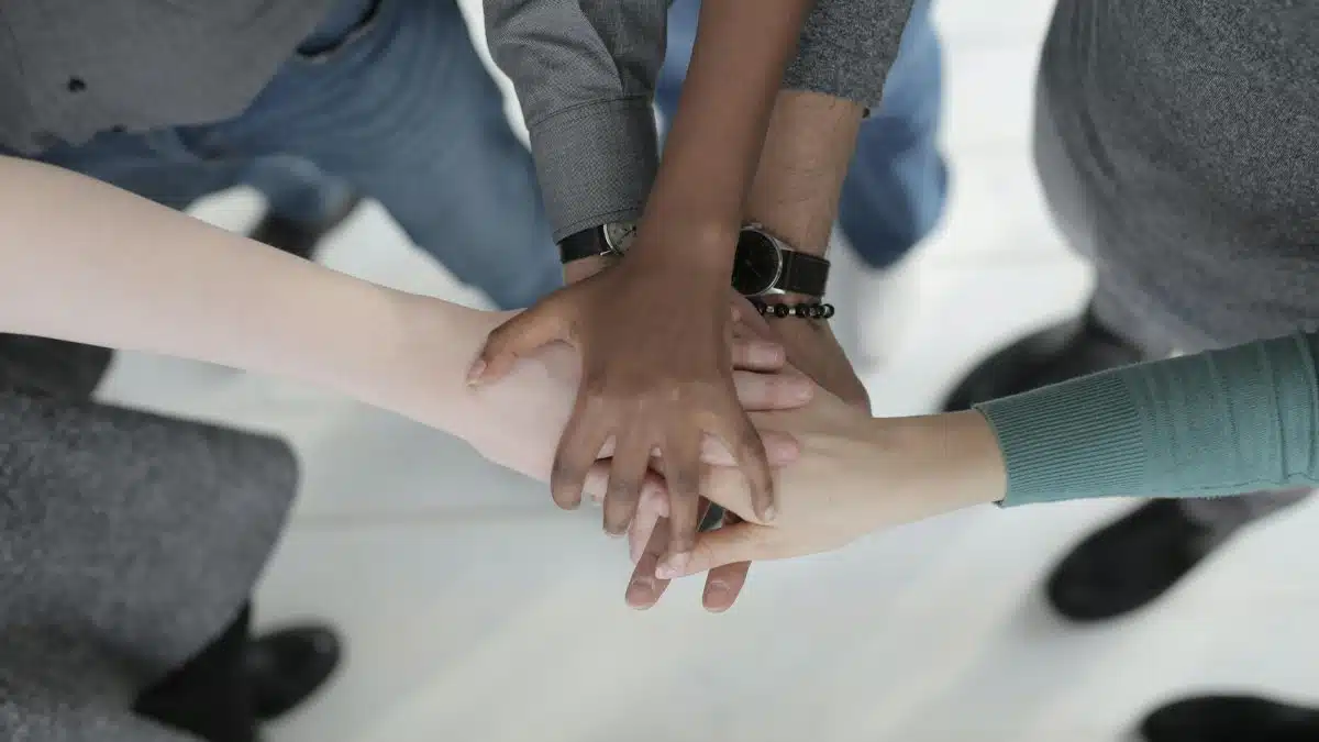 Crop from above of faceless multiracial friends in casual clothes uniting hands after coming to agreement while standing on light grey ceramic floor