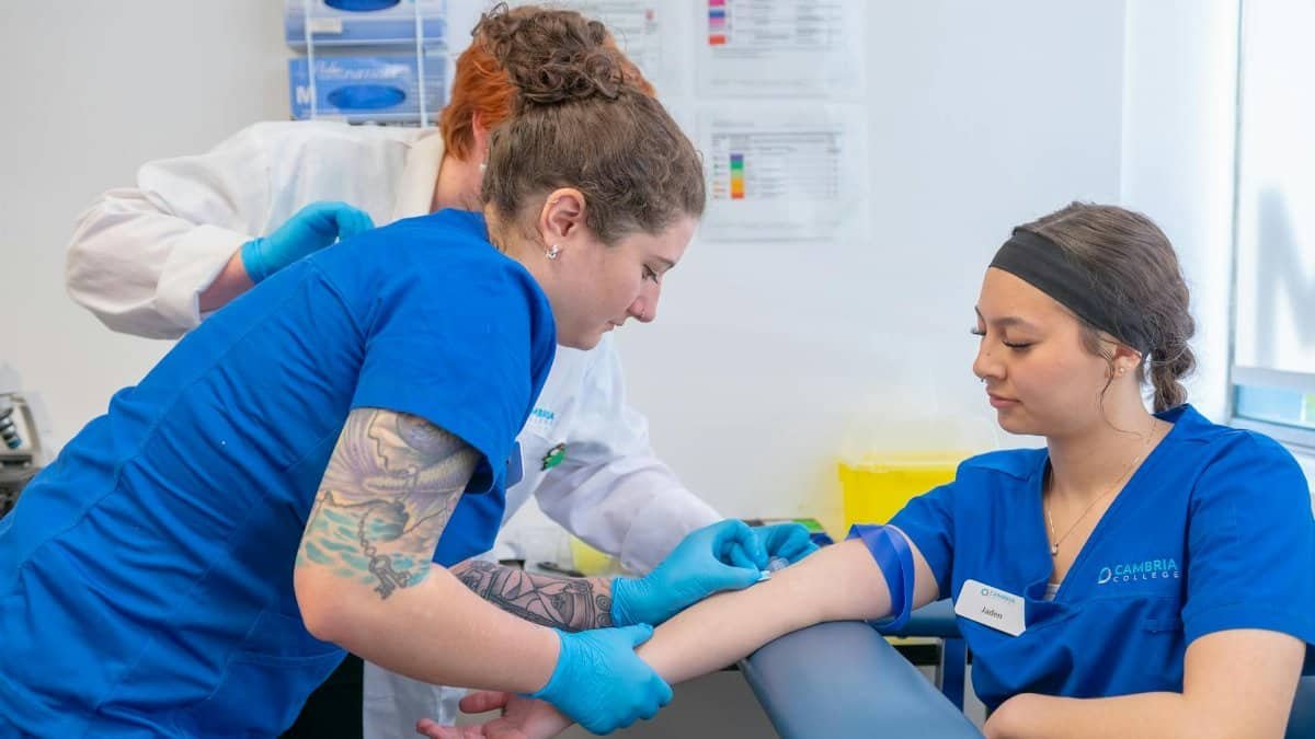Nurses and a medical student practice blood draw in a clinical setting.