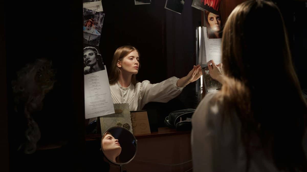 An actress adjusts her script in front of the dressing room mirror, preparing for her performance.
