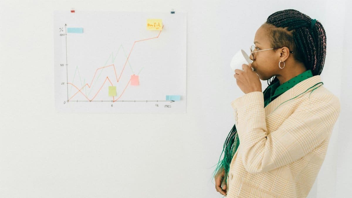Professional woman in office attire drinking coffee while analyzing a financial graph indoors.
