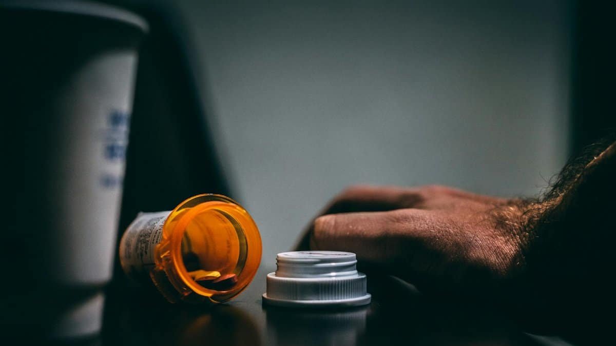 Moodily lit scene of an open prescription bottle and hand on a table, depicting healthcare themes.