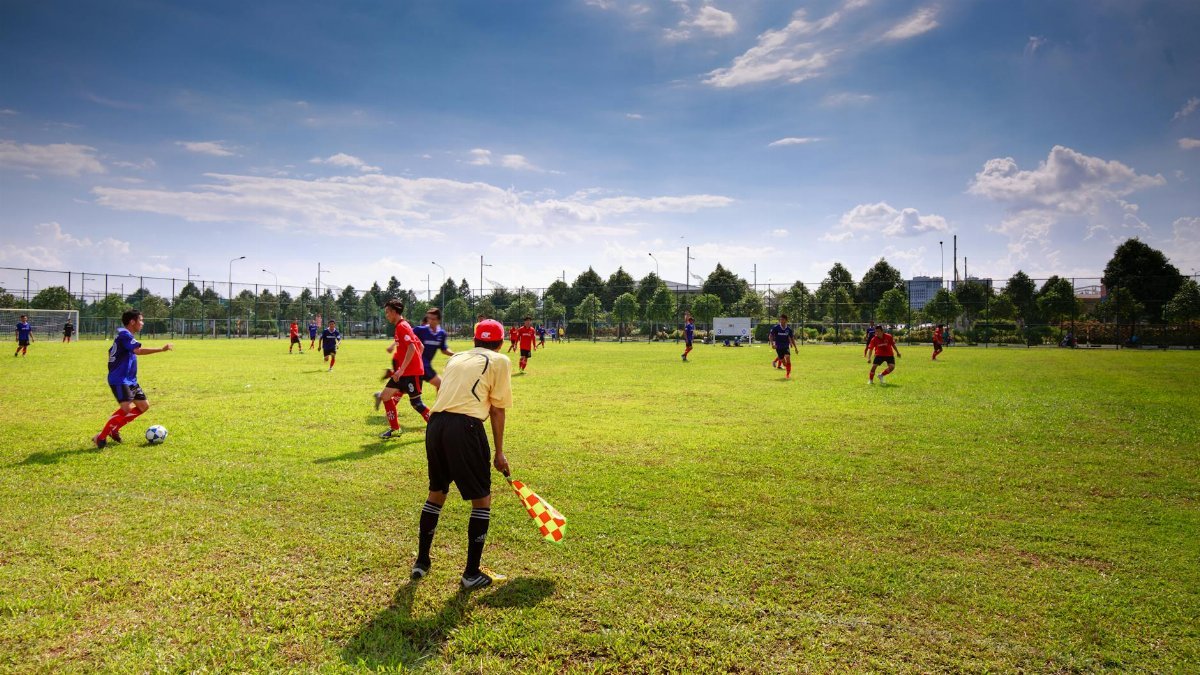 Youth soccer match in outdoor field with players, referee, and clear sky.