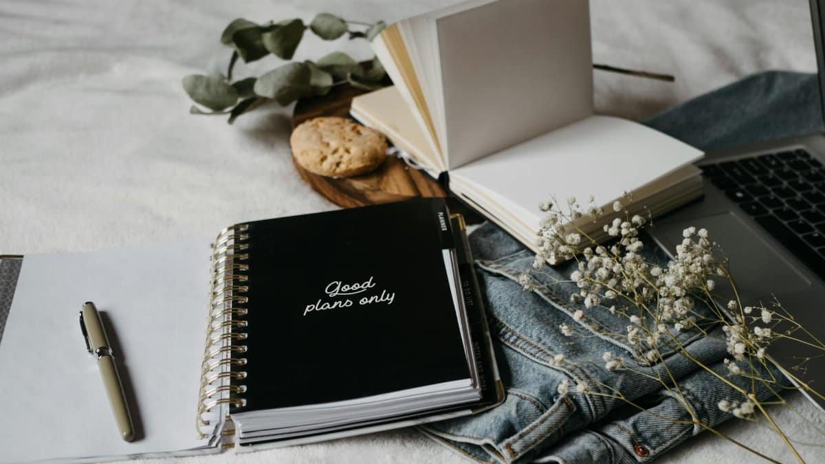 Aesthetic workspace with a notebook, pen, flowers, and laptop on a cozy surface.