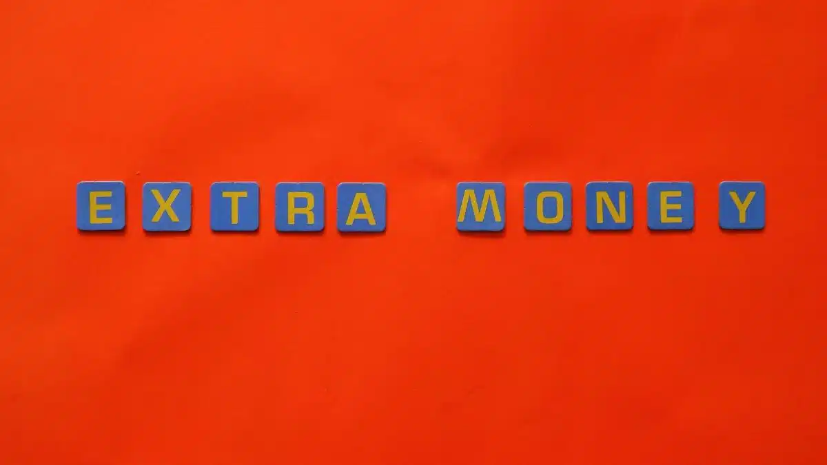 Bright orange background with 'EXTRA MONEY' spelled in blue and yellow tiles, illustrating financial concepts.