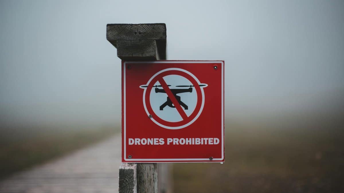 Sign prohibiting use of drones placed on wooden fence near wooden walkway in field in foggy day