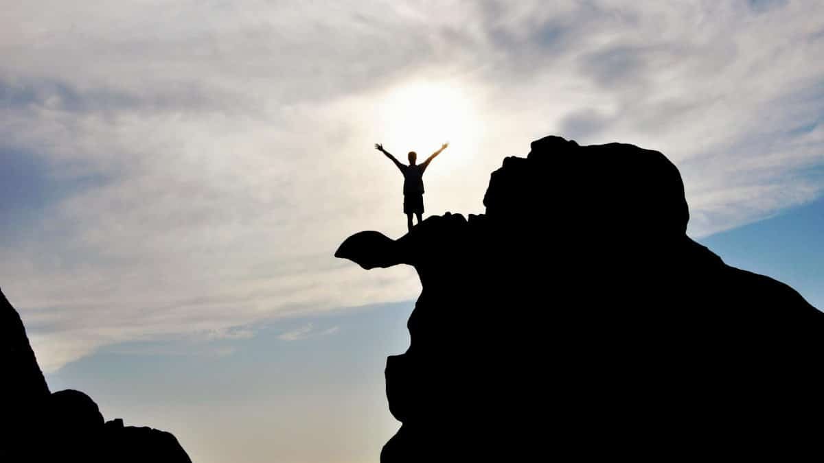 Silhouette of a person celebrating on a mountain peak against a dramatic sky, symbolizing freedom and success.