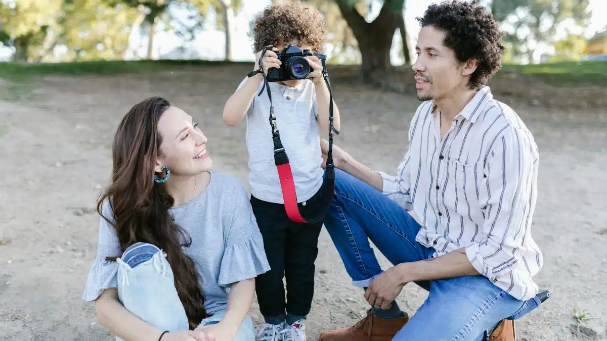 A child takes a photo of smiling parents, capturing family moments in a park setting.