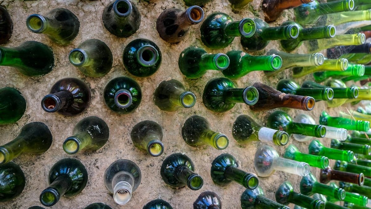 A creative wall made from recycled colored glass bottles arranged artistically outdoors.
