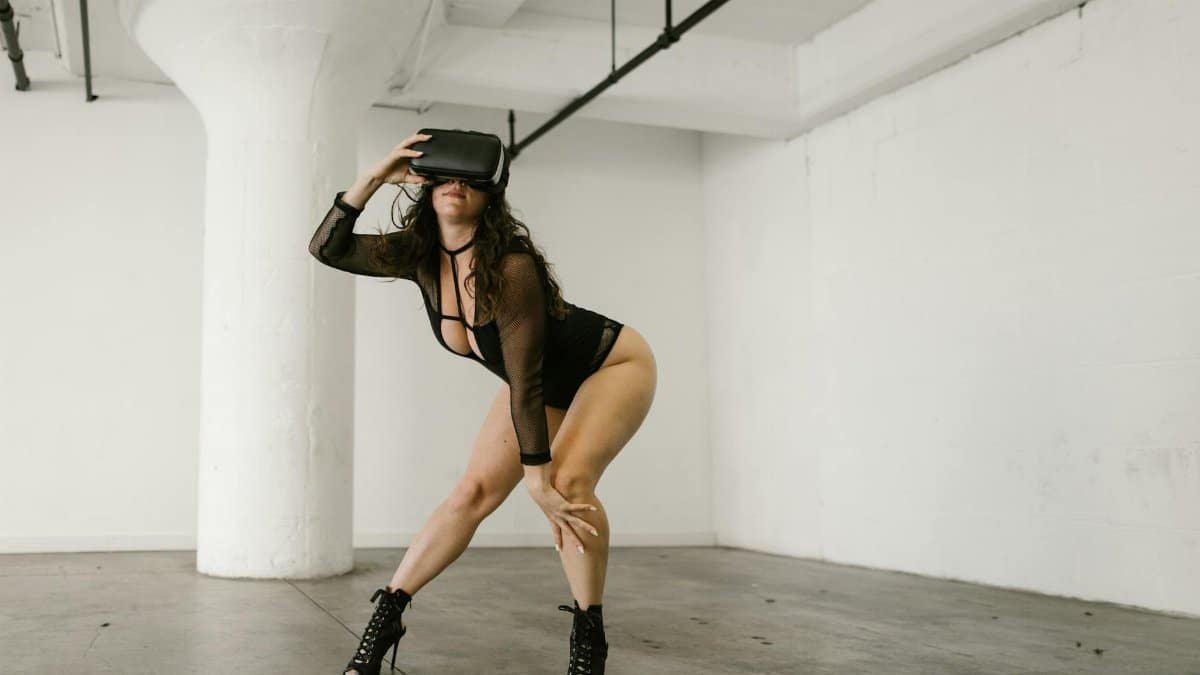 A woman in a stylish outfit dances while wearing a virtual reality headset in an industrial indoor space.