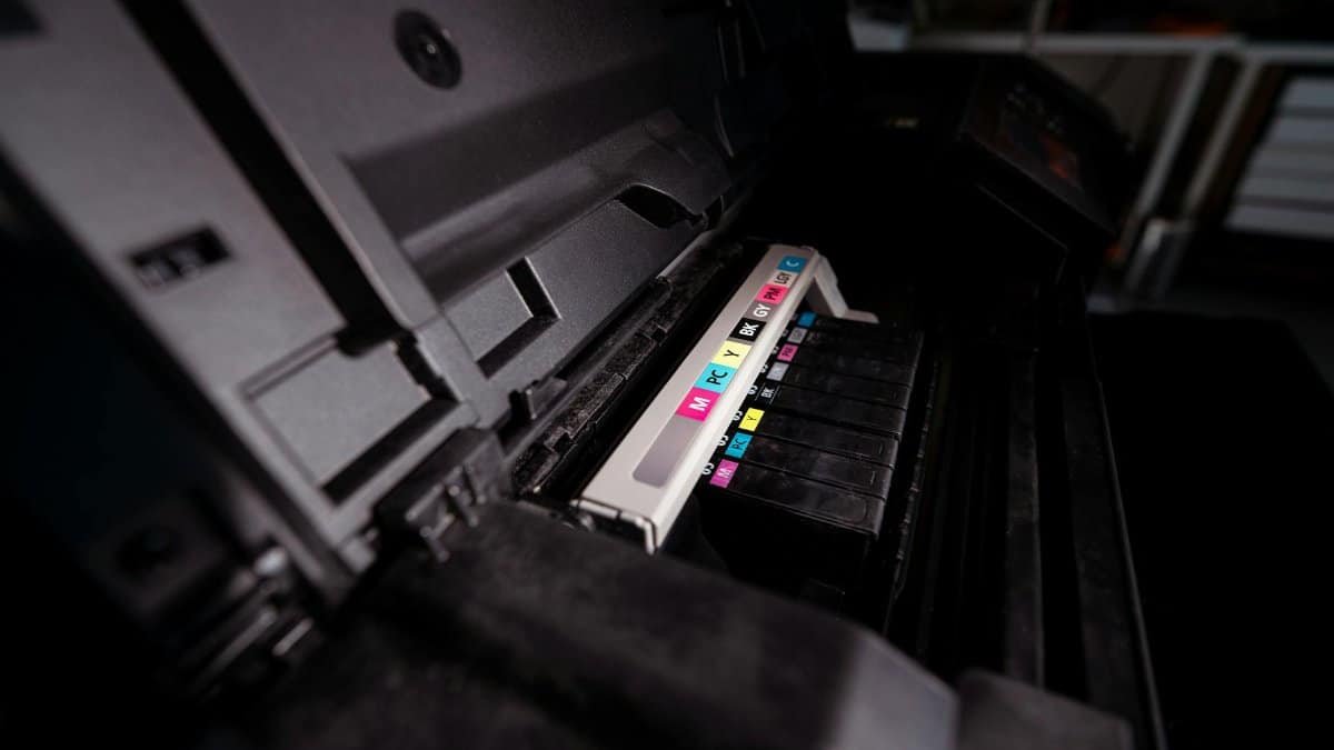 Detailed view of open printer with visible CMYK ink cartridges in a dark setting.