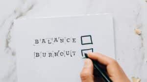 Close-up of a hand hovering over a checklist with options for balance or burnout, symbolizing stress and choice.