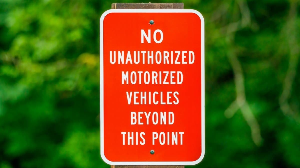 A red sign warns of no unauthorized motorized vehicles in a green forest setting.