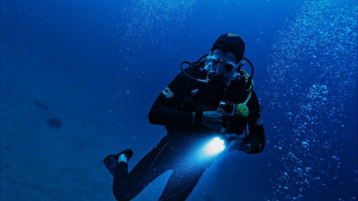 A scuba diver exploring the deep ocean with a flashlight, surrounded by bubbles and marine life.