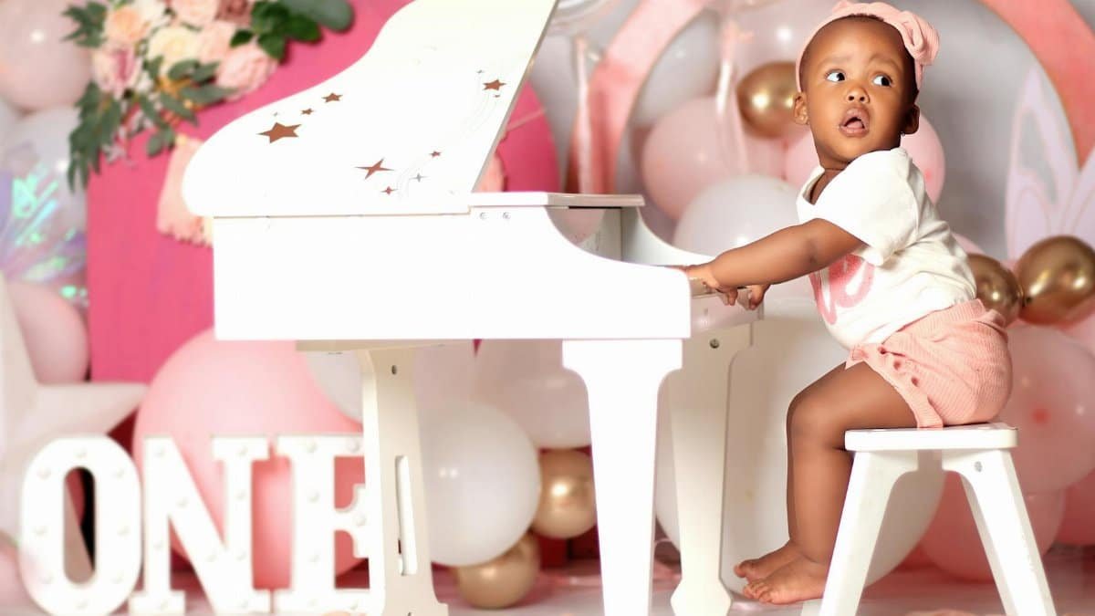 Baby celebrating first birthday with toy piano and festive decorations.