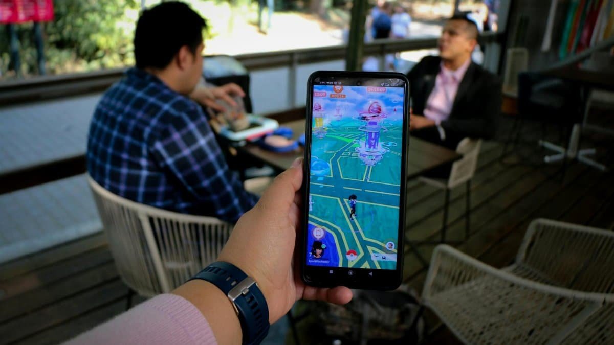 Person playing mobile game in a cafe with social interaction shown in the background.