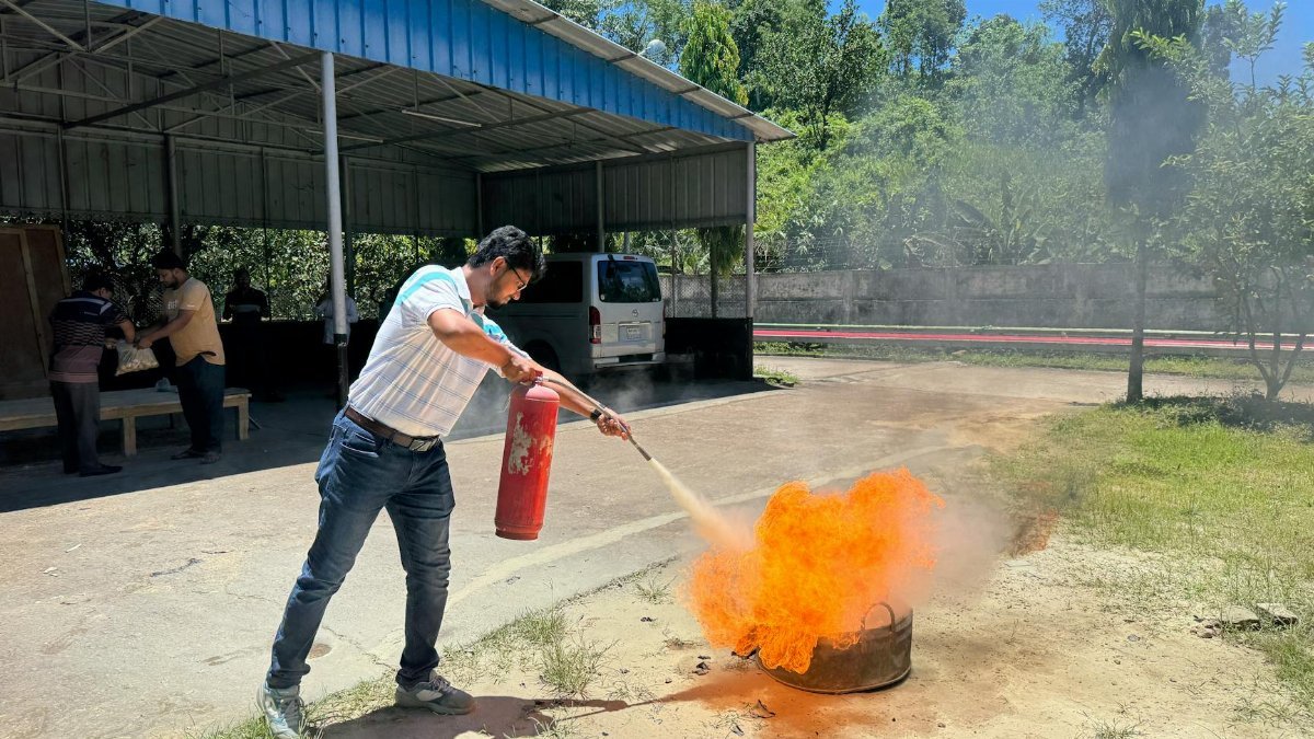 A man uses a fire extinguisher to put out a controlled fire during an outdoor safety training session.
