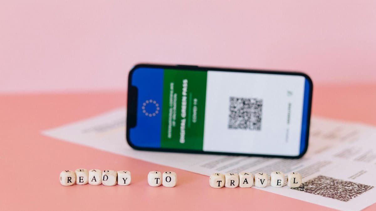 Smartphone displaying digital green pass on a pink surface with travel beads.