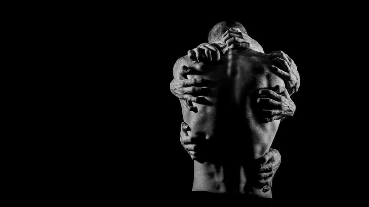 A powerful black and white image depicting multiple hands grasping a man's bare back, symbolizing complex emotions.