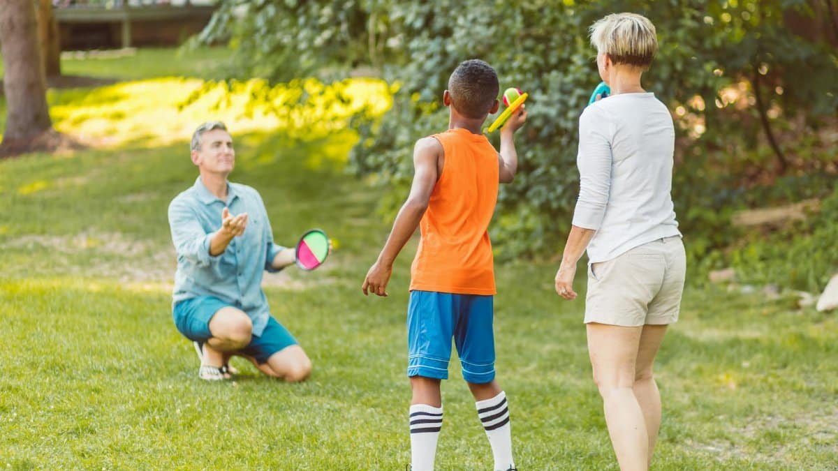 A family enjoying a game of velcro ball in a sunny park, showcasing togetherness and fun.