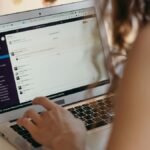 A businesswoman typing on a laptop in an office setting, using Slack for communication.
