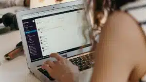 A businesswoman typing on a laptop in an office setting, using Slack for communication.