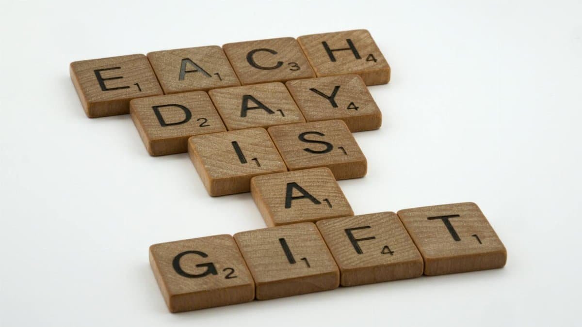 Scrabble tiles spelling 'Each Day is a Gift' on a white background, conveying positivity and inspiration.