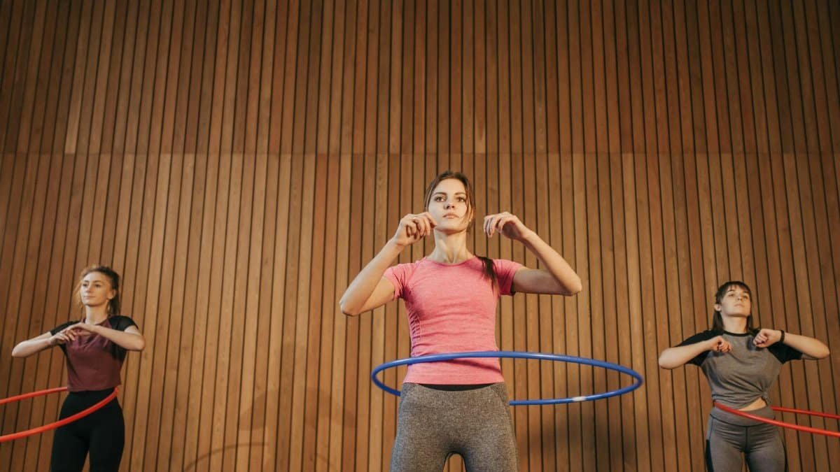 Three women exercising with hula hoops indoors promoting fitness and fun.