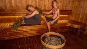 Two people enjoying a traditional sauna session with whisking branches in a modern Nordic design space.