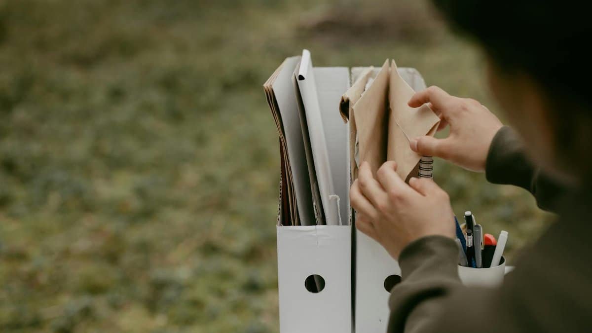 Person sorting documents in folders outdoors, hands visible, neutral tone.