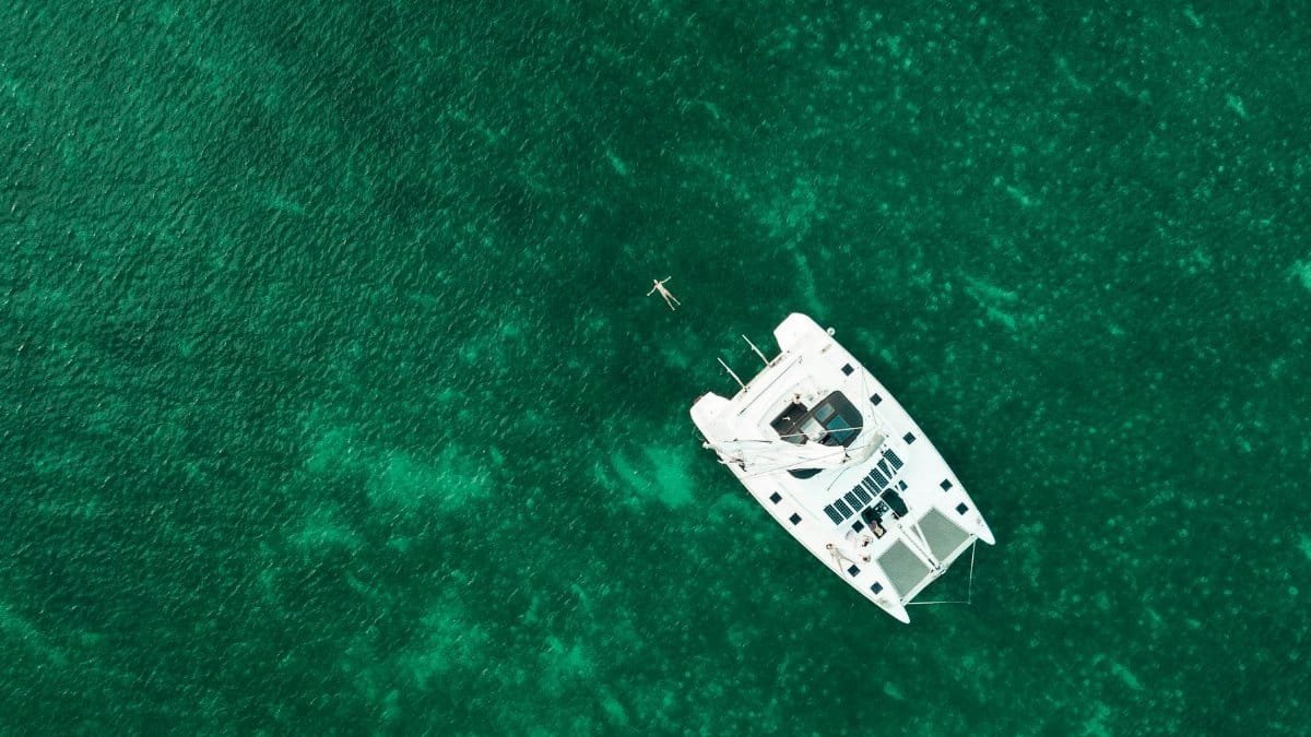 Drone captures serene yacht floating in idyllic emerald sea, perfect for travel inspiration.