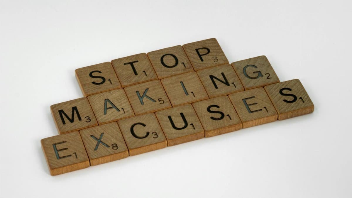 Wooden Scrabble tiles spell 'Stop making excuses' on a white background, encouraging self-improvement.