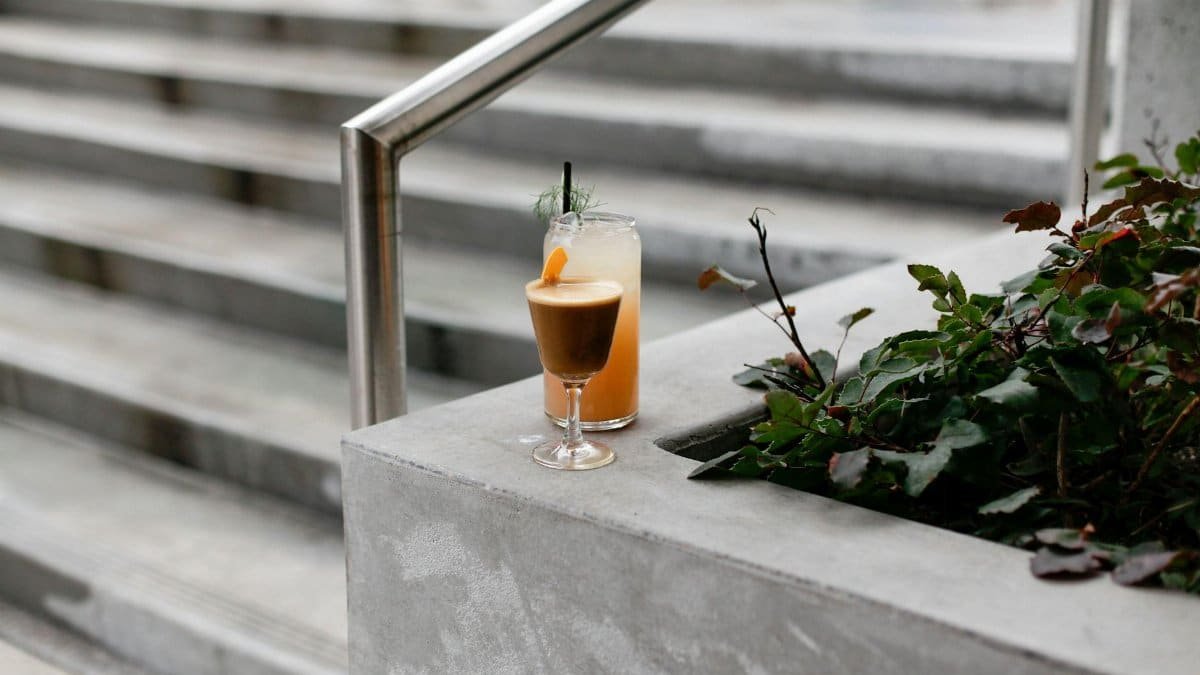 Two beverages on concrete in Seattle: a coffee and a juice next to greenery and steps.
